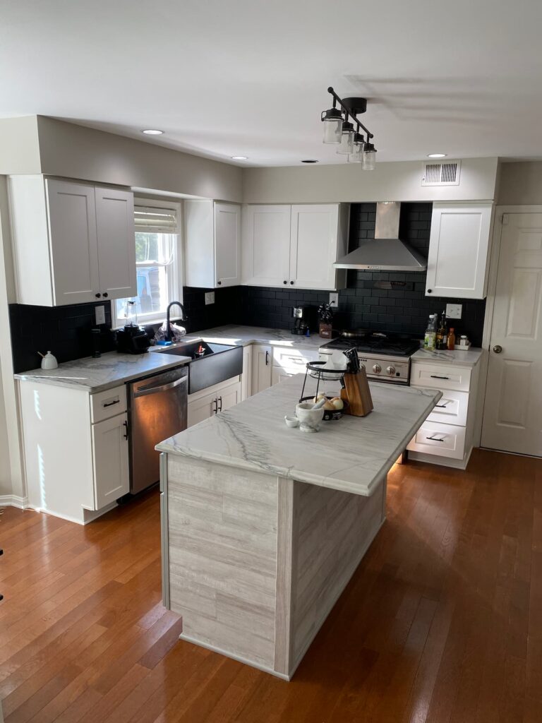Modern kitchen with white cabinets, black backsplash, stainless steel appliances, marble countertops, and a central island on a wood floor.