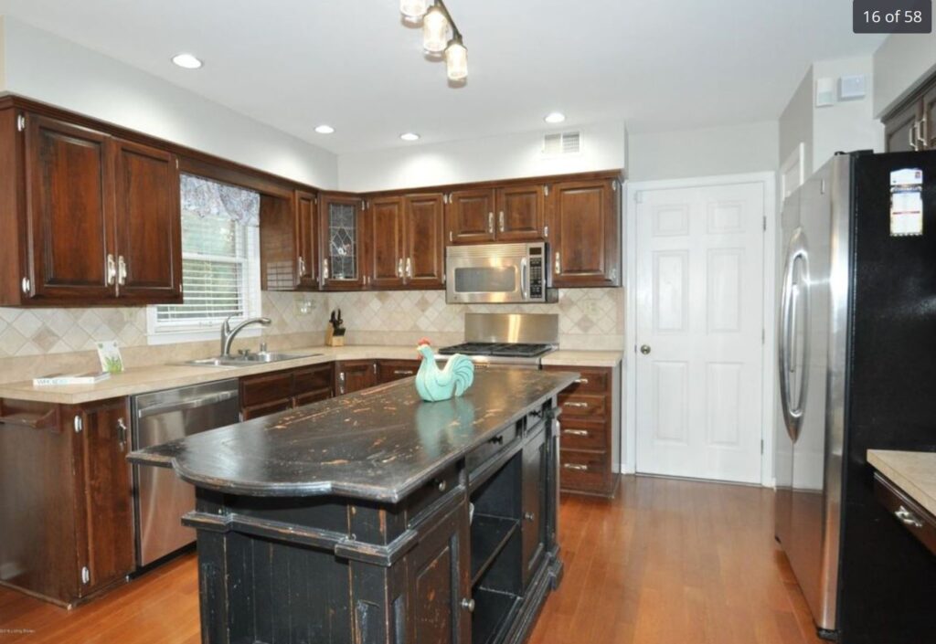 Modern kitchen with dark wood cabinets, stainless steel appliances, a black island with a decorative rooster, tile backsplash, and hardwood floors.