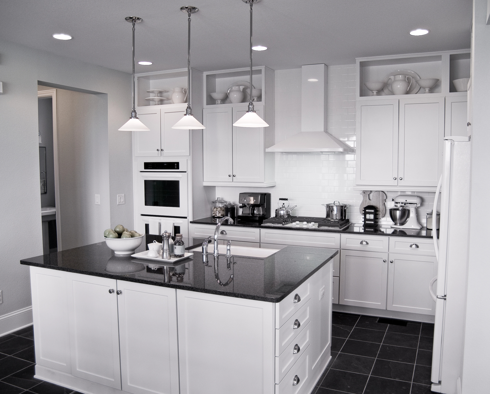Modern kitchen with white cabinets, black countertops, stainless steel appliances, an island with a sink, and pendant lights hanging from the ceiling.